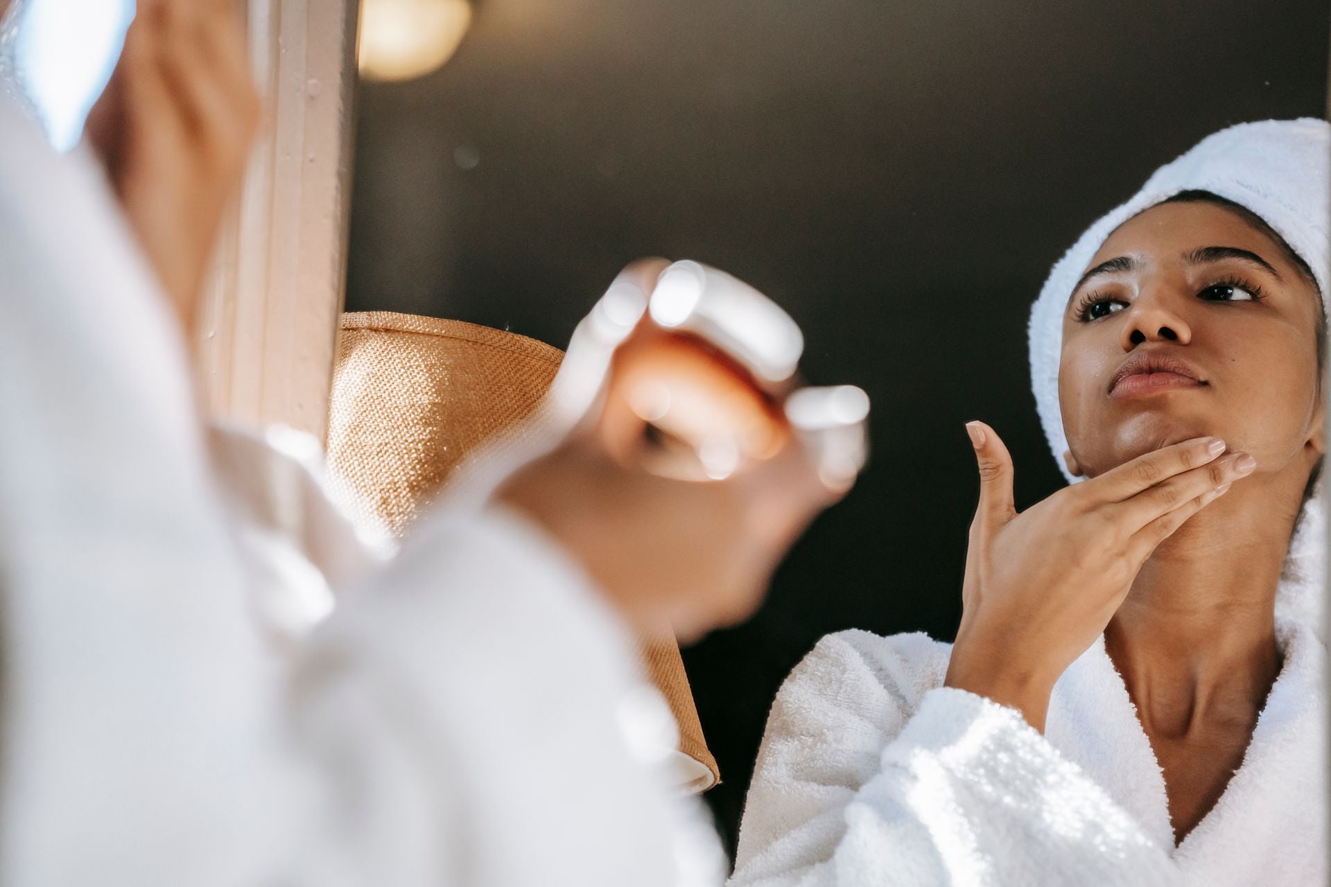 Woman in a bathrobe applying moisturiser while looking in the mirror